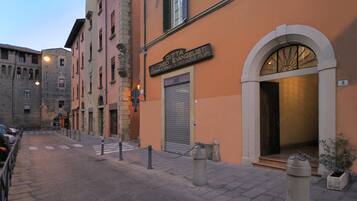 A street view with a building featuring a closed shutter and a sign with Italian text.
