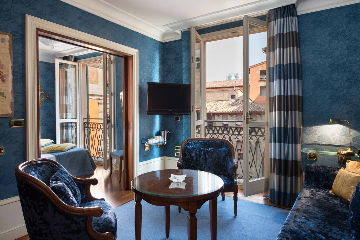 Une pièce avec un mur bleu, un lit, une télévision, une table et un canapé.