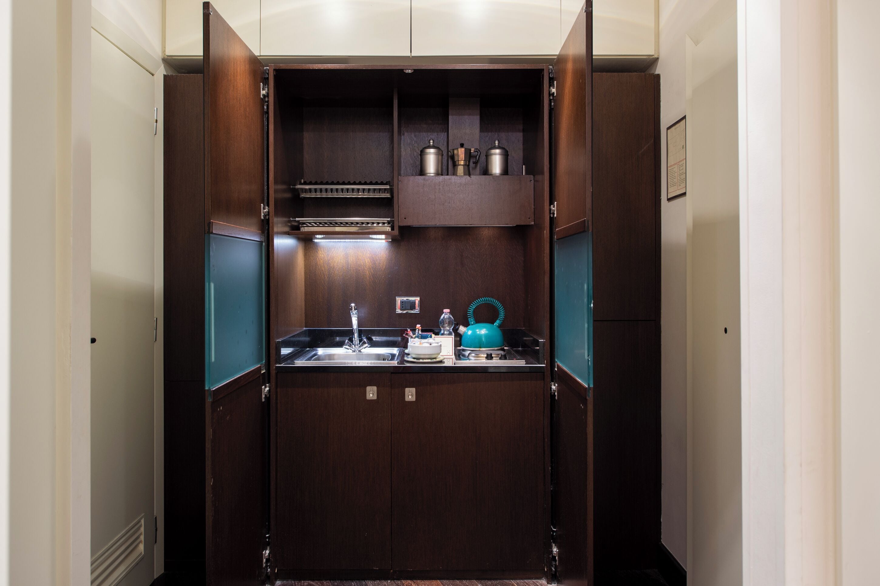 A compact kitchen with a sink, a kettle, and storage cabinets.