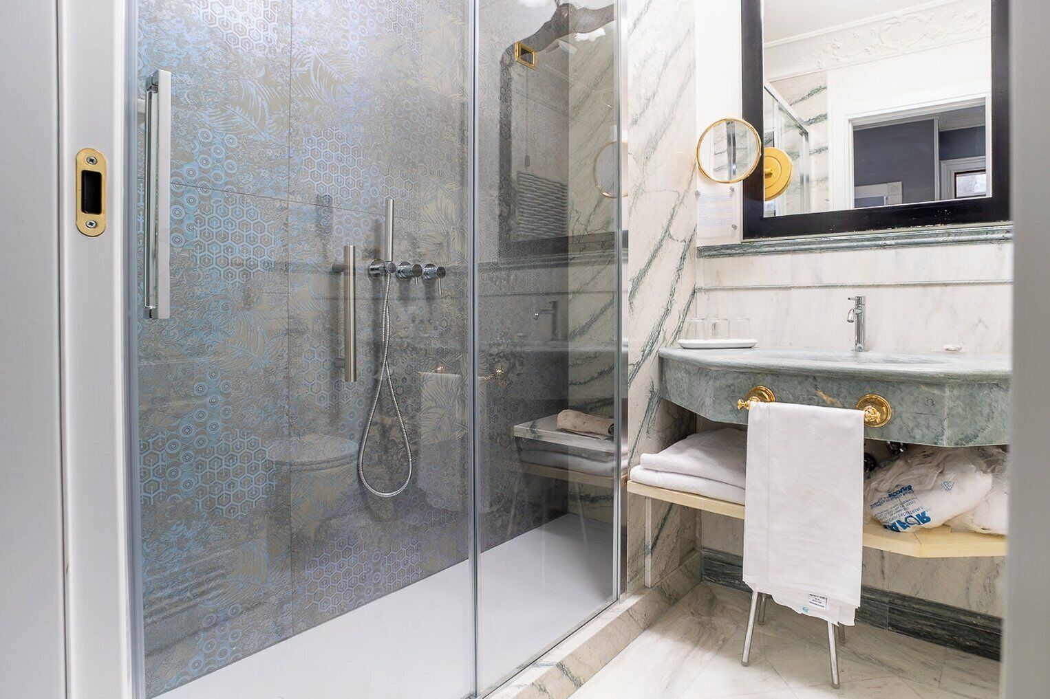 Un baño moderno con ducha acristalada, lavamanos de mármol y un espejo grande.