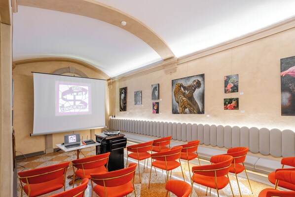 A conference room with a projector screen displaying a hotel sign, a laptop, and a sound system. The room has red chairs and artwork on the walls.