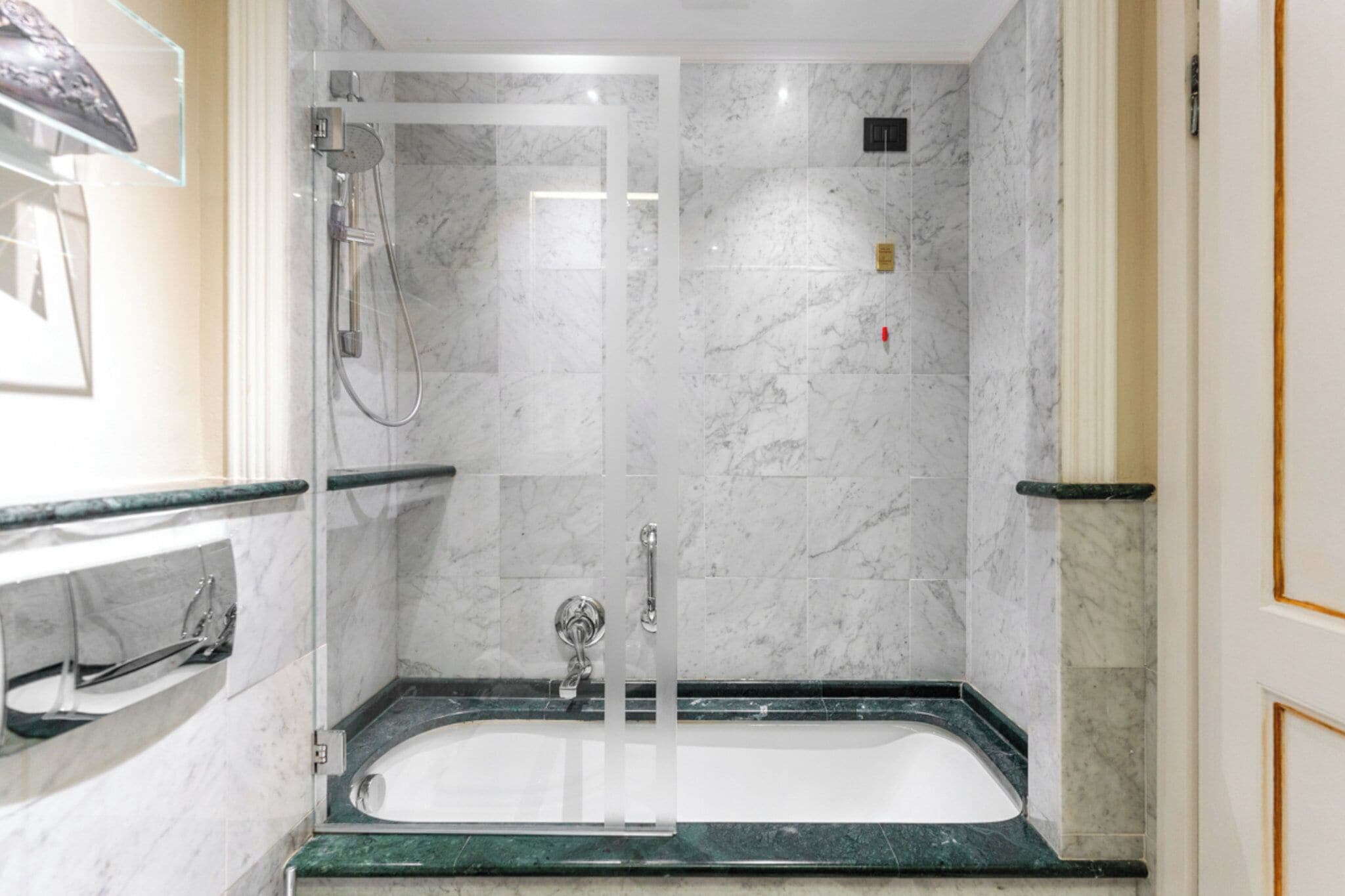 A modern bathroom with a glass-enclosed shower, a standalone bathtub, and a marble-tiled wall.