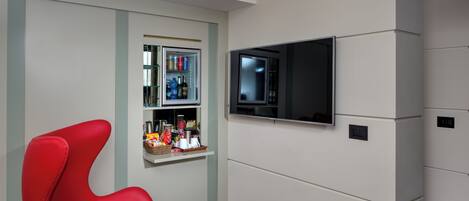 A modern living room with a red chair, a television mounted on the wall, and a small shelf with various items.