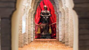 Un modello di cavaliere in armatura seduto su un trono, circondato da un drappo rosso, all'interno di un arco in pietra.