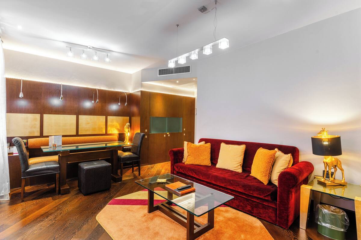 Un salon moderne avec une table basse en verre, un canapé rouge, un bureau avec une chaise et une lampe.