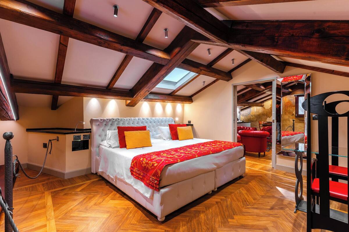 Une chambre spacieuse avec un grand lit, des poutres apparentes et une lucarne.