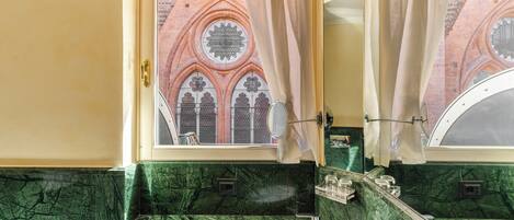 A bathroom with a green marble sink, a mirror, and a view of a brick building through a window with a curtain.
