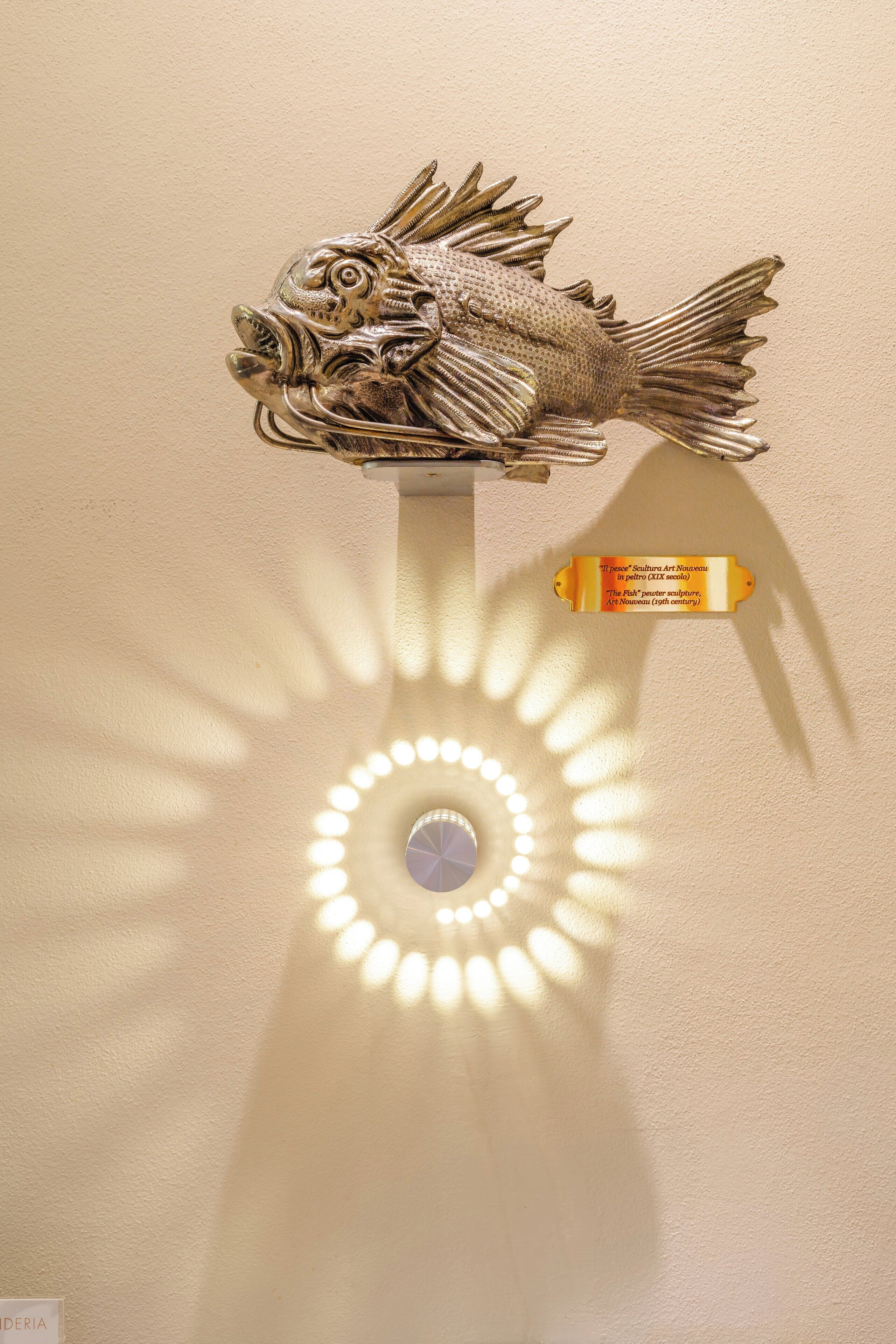 A fish sculpture mounted on a wall with a spotlight casting a shadow.