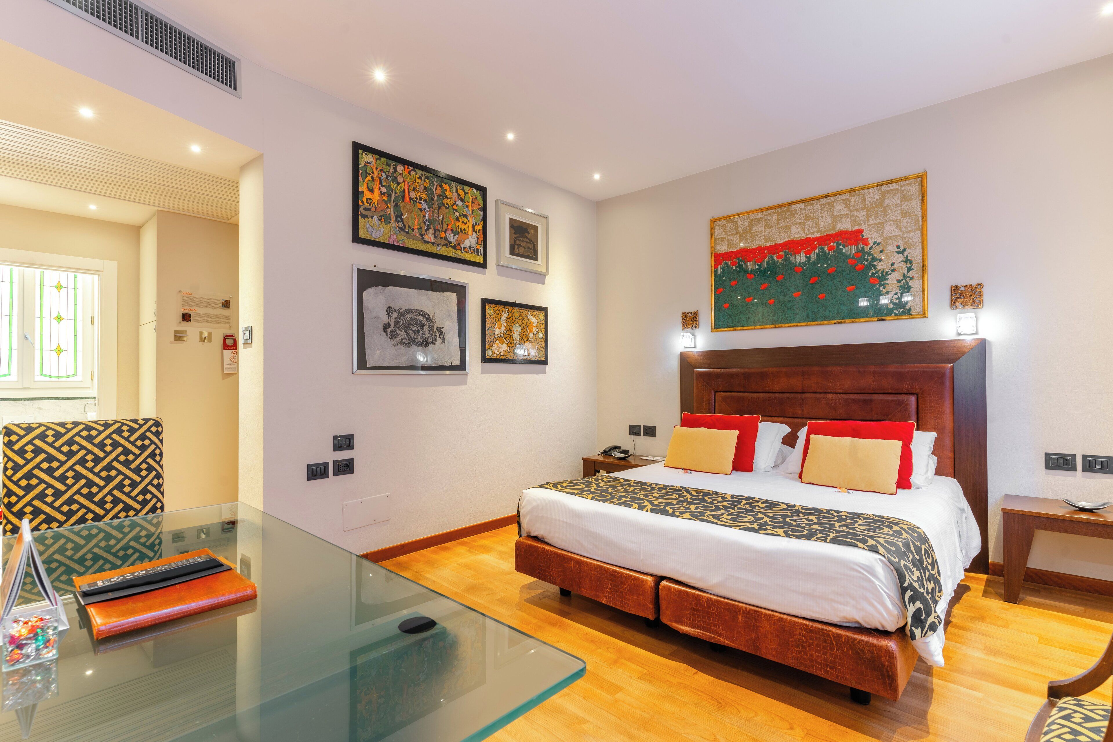 A modern hotel room with a large bed, a glass table, and artwork on the walls.
