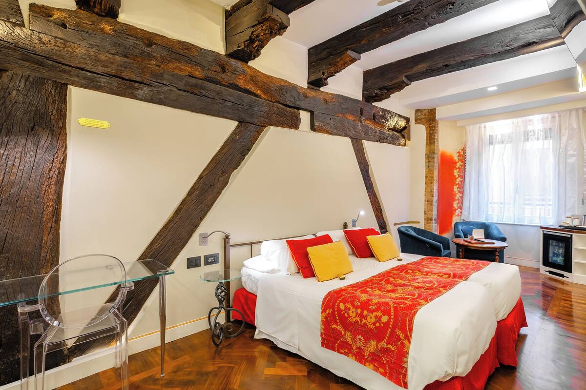 Une chambre avec un grand lit, des poutres en bois, une table en verre et une chaise.