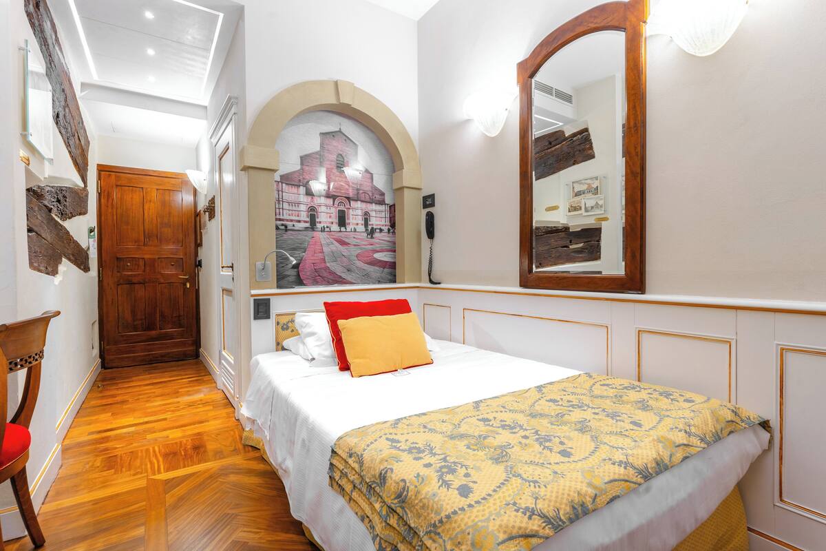 Une chambre d’hôtel avec un lit, une porte en bois, un miroir et une fresque murale.