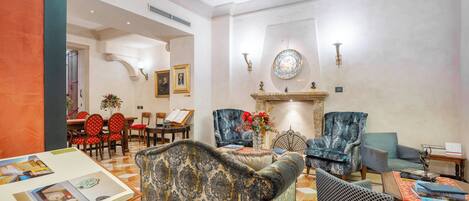 A spacious living area with a fireplace, patterned sofas, and a dining area with red chairs.
