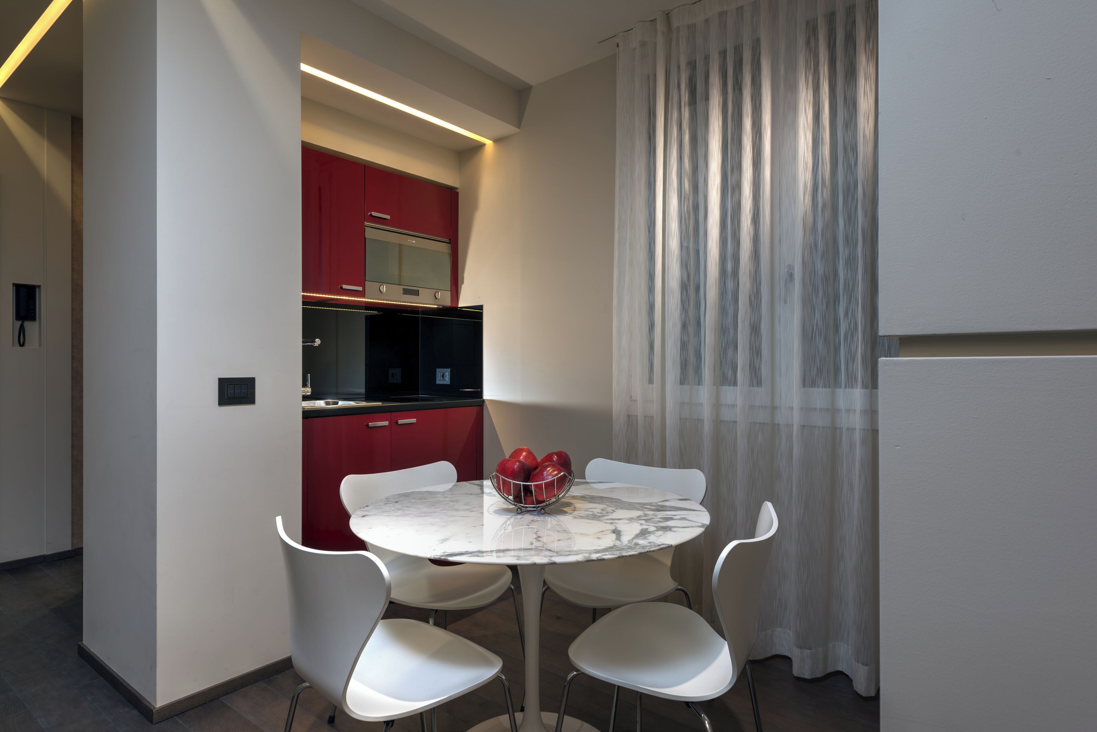 Una cocina moderna con armarios rojos, una mesa de mármol blanco y cuatro sillas blancas.