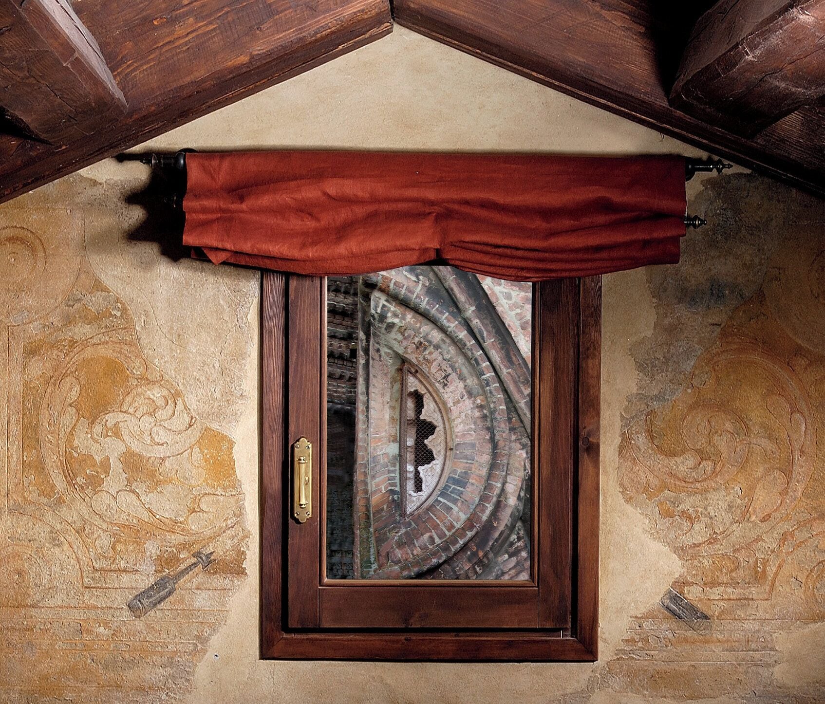 A window with a wooden frame and a brass handle, set in a stone wall with decorative carvings.
