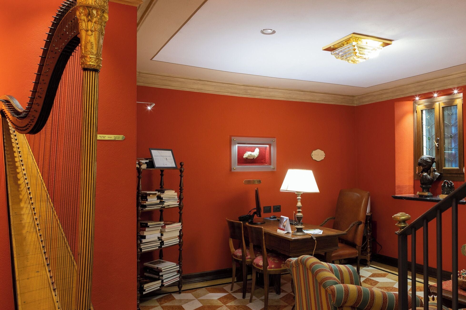 Una habitación con un arpa, un escritorio con lámpara, una silla y una estantería.