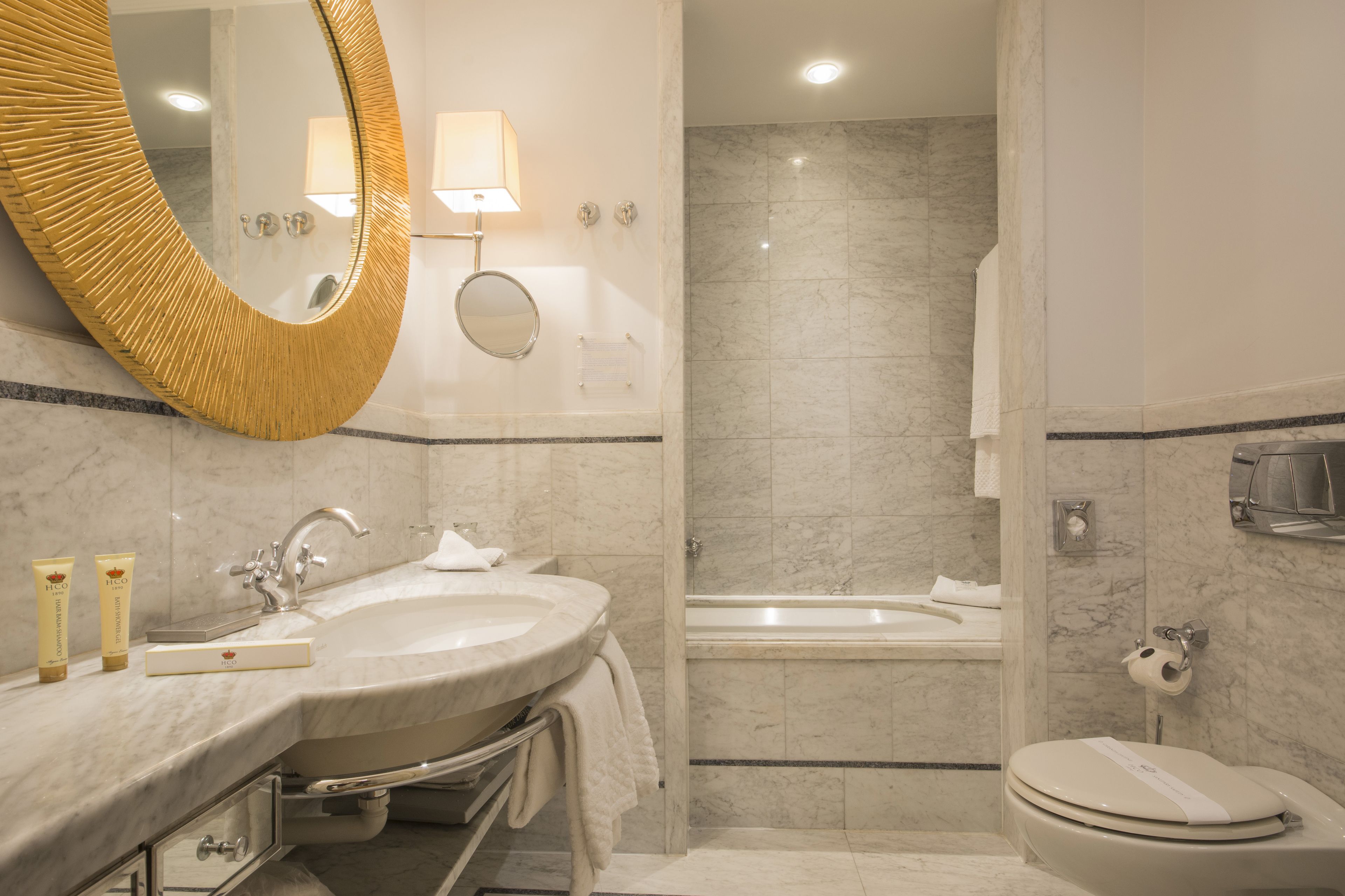 A modern bathroom with a large oval mirror, a sink, a bathtub, and a toilet.
