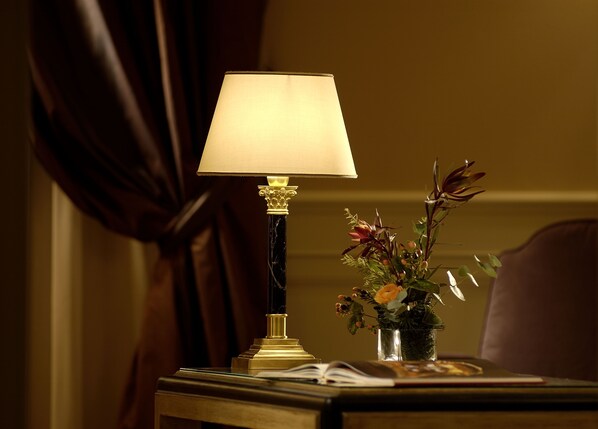 A lamp with a white shade, a vase with flowers, and an open book on a bedside table. - Hotel Corona d'Oro (Bologna)