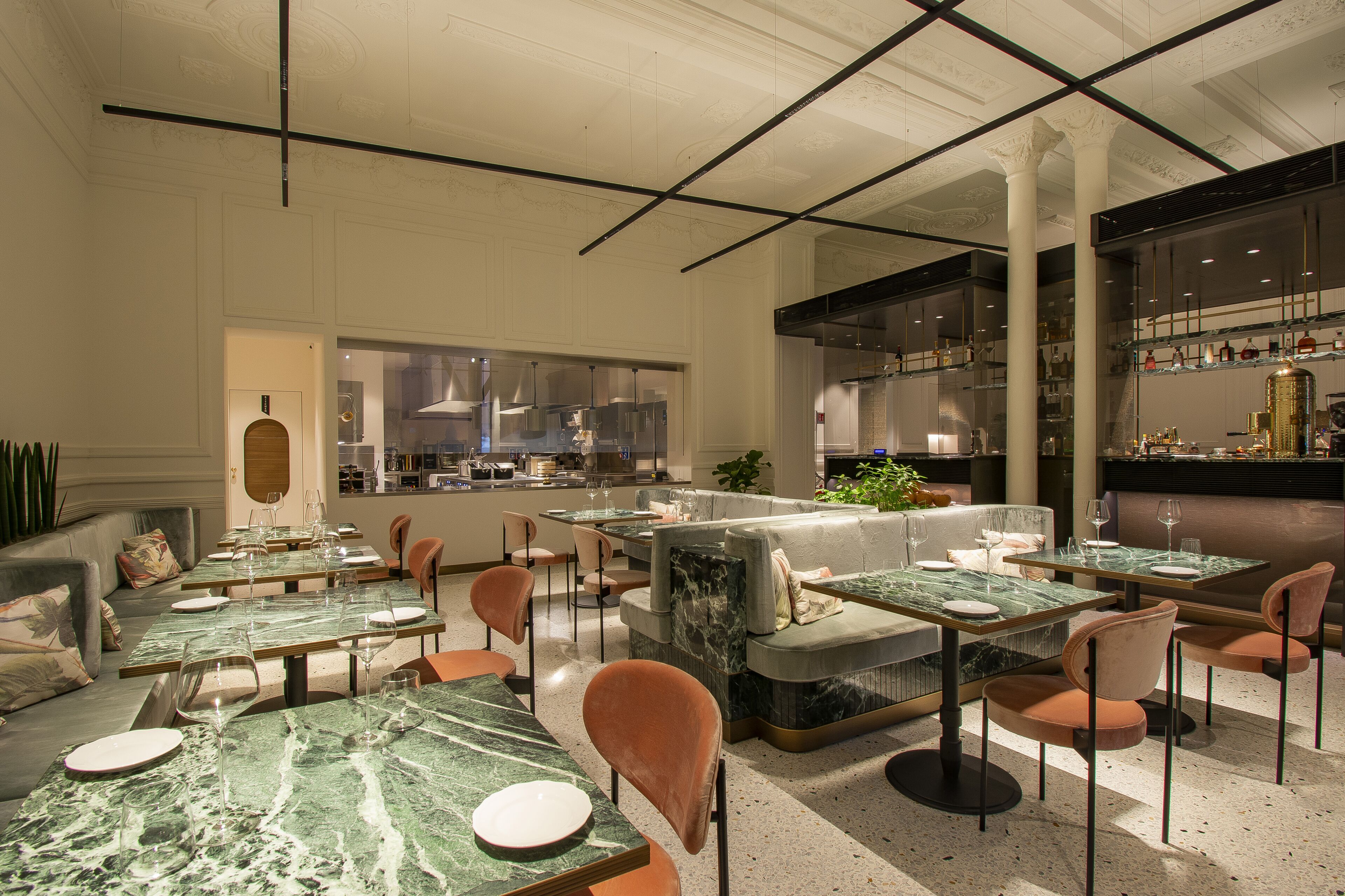 A modern restaurant with marble tables, cushioned seating, and a bar area.