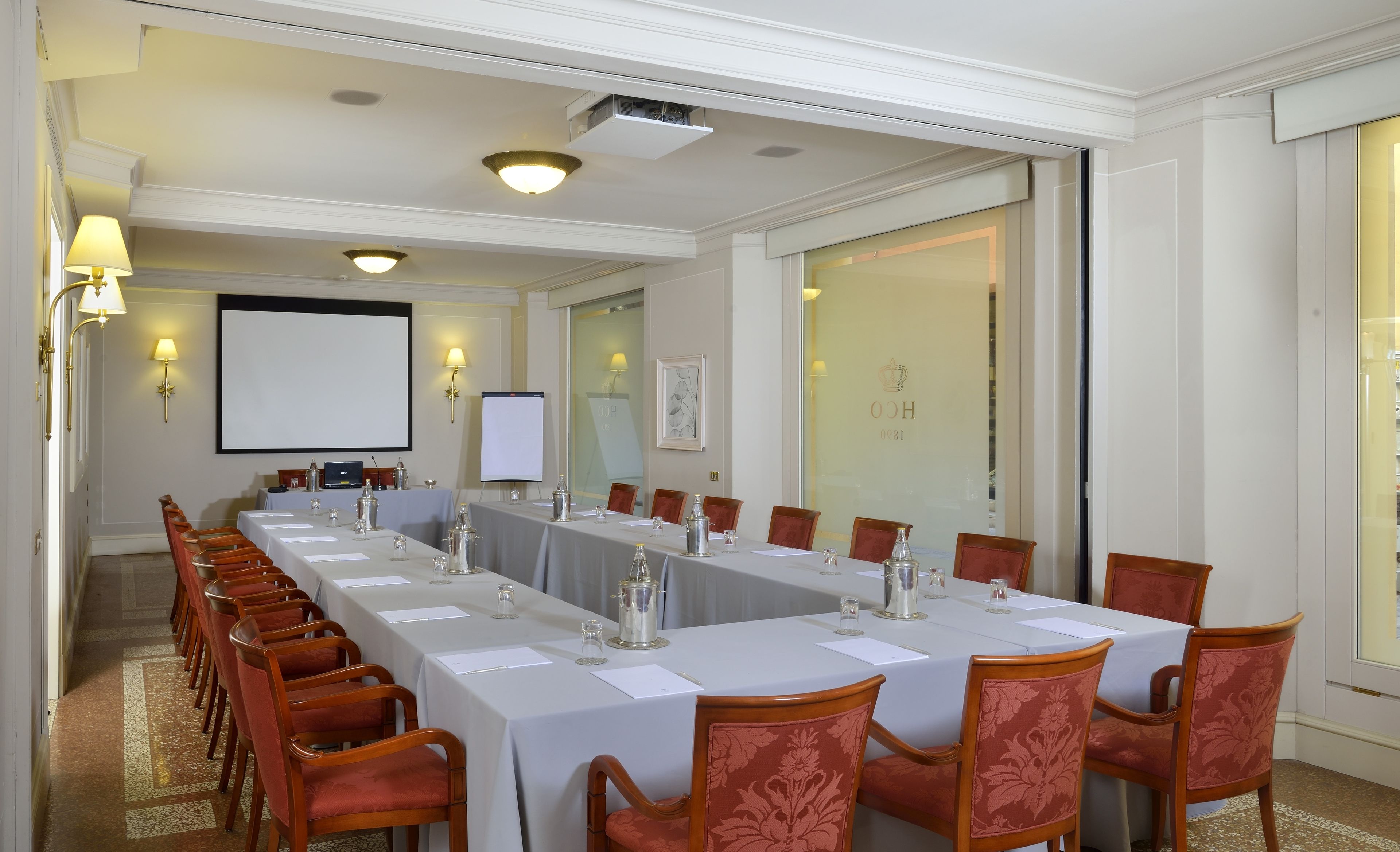 A conference room with a long table, chairs, a projector screen, and a large window.