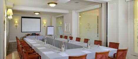 A conference room with a long table, chairs, a projector screen, and a large window.