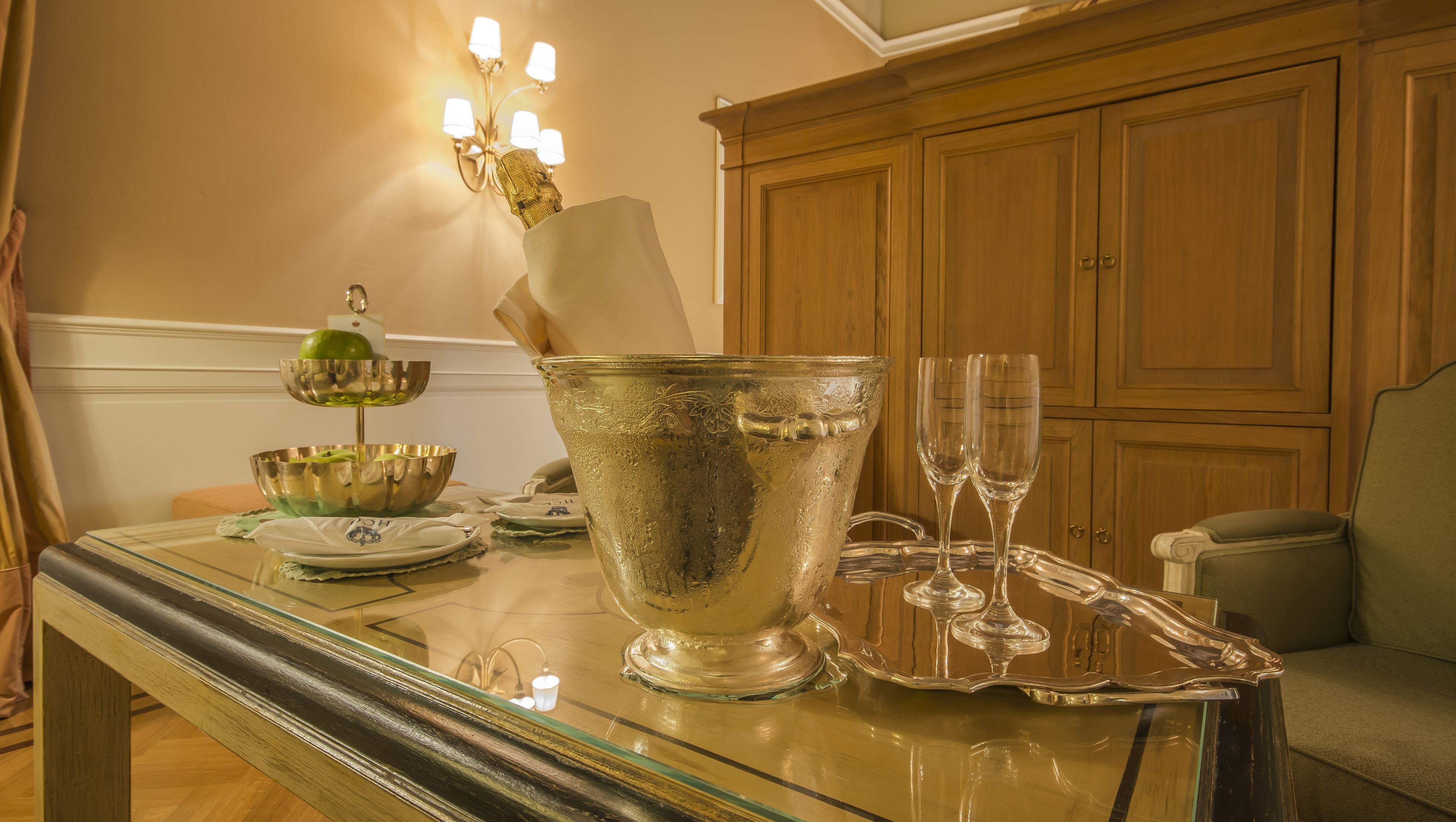 A dining table with a large silver pitcher, two glasses, and a green bowl.