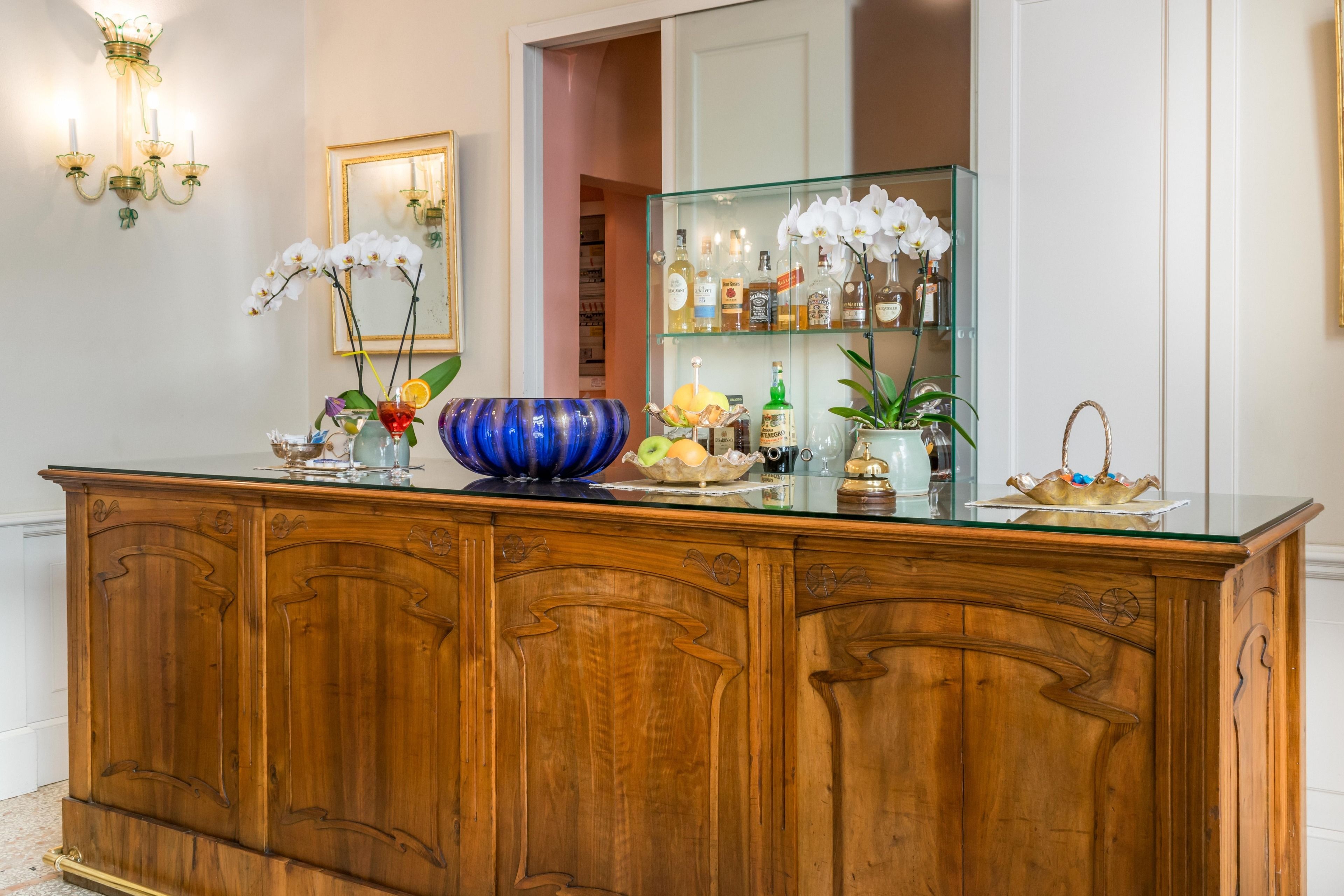 Un bancone in legno con piano in vetro, decorato con orchidee, un vaso blu e diverse bottiglie.