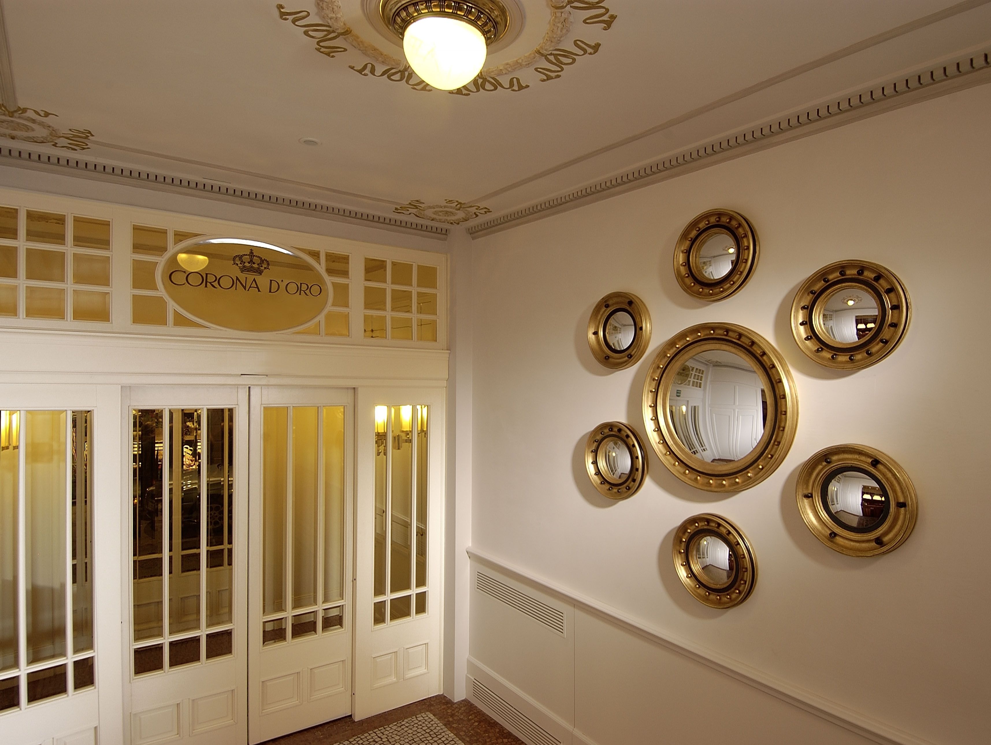 A hotel lobby with a double door entrance, a large mirror on the wall, and a sign above the doors.