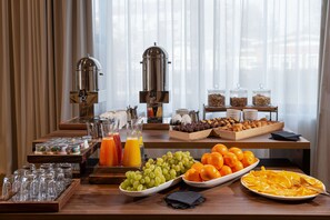 Un bufé de desayuno con diversas frutas, jugos y cafeteras.