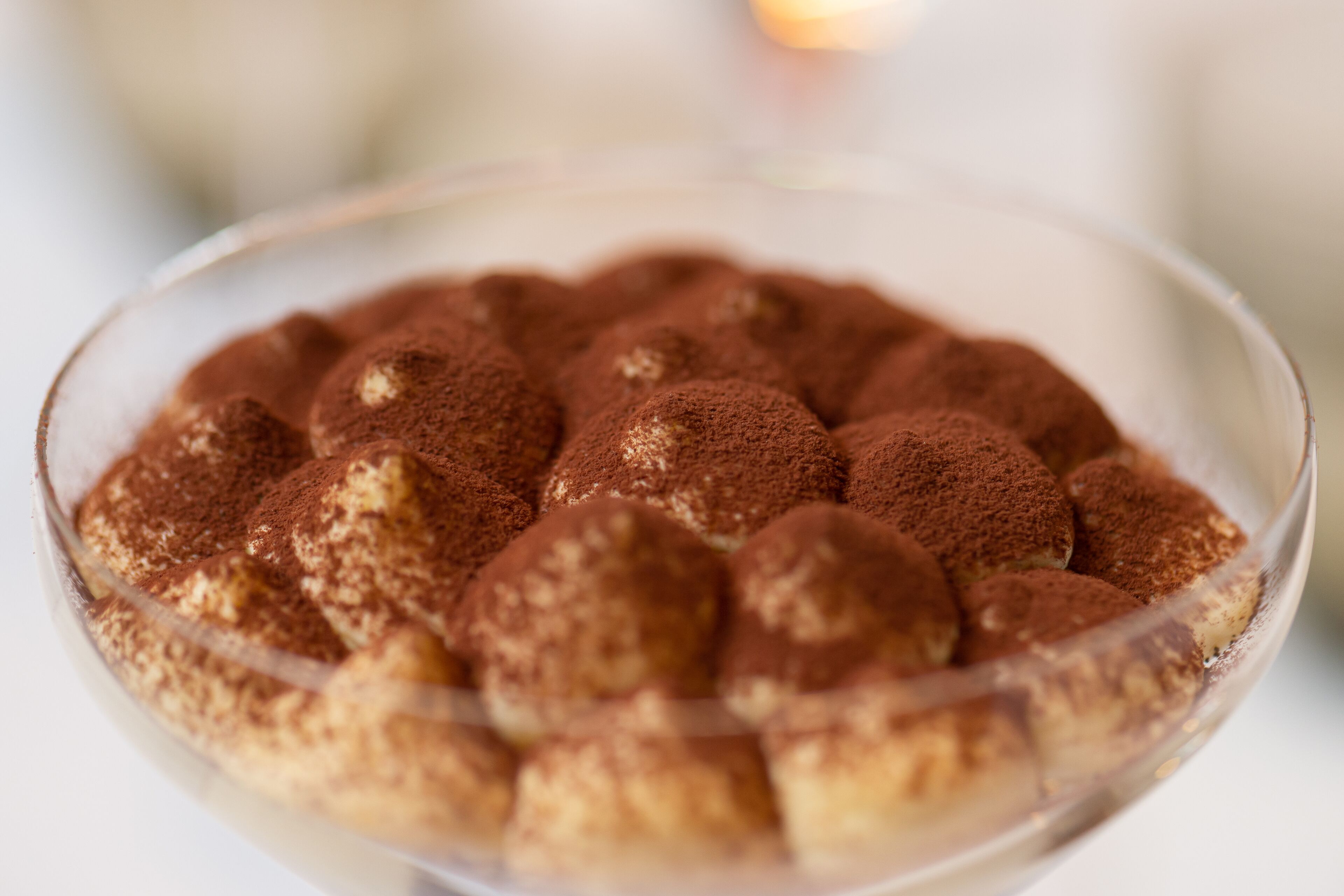 A clear glass bowl containing a dessert with a dusting of cocoa powder on top.