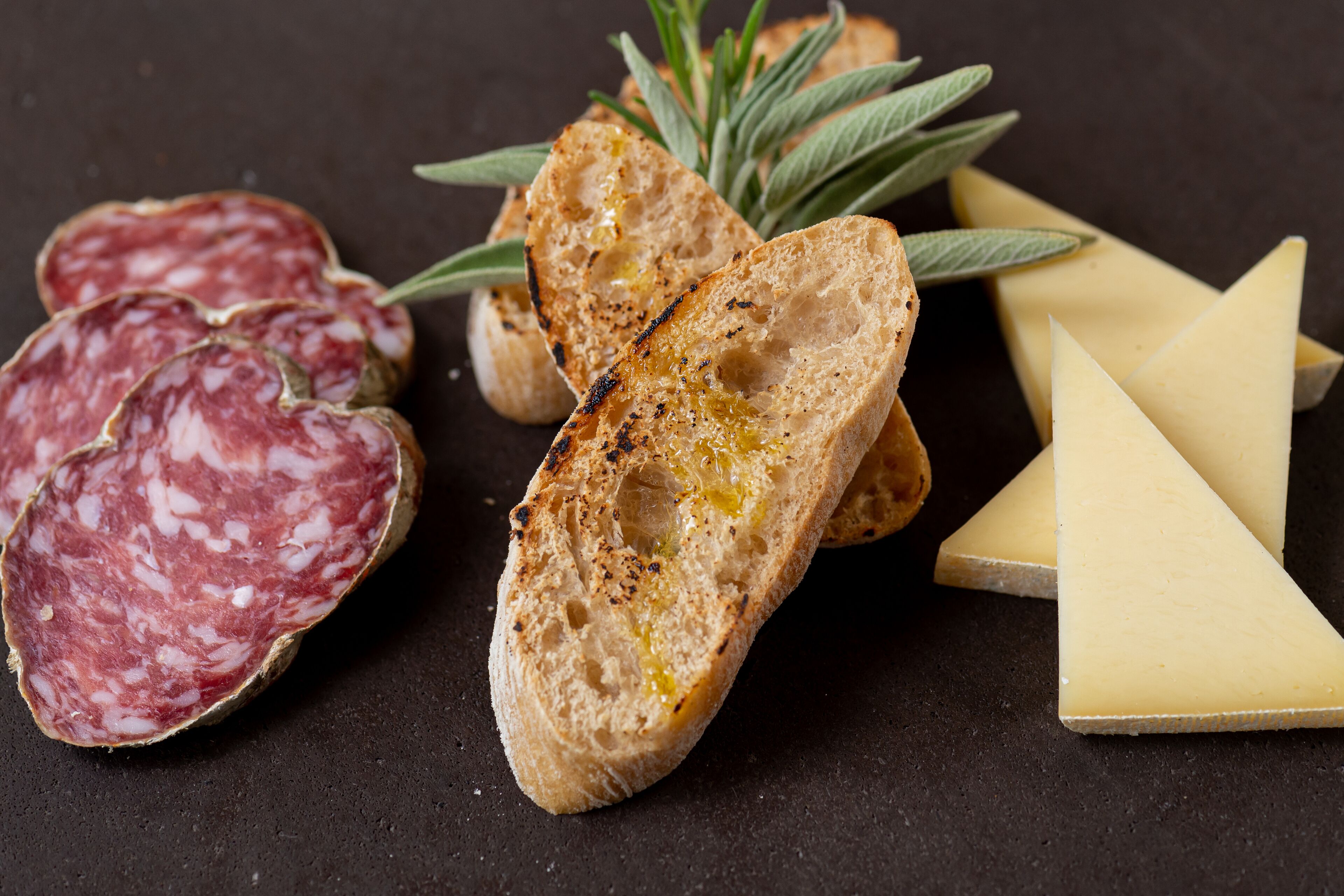 Des tranches de salami, du pain grillé et du fromage, le tout disposé sur une surface sombre.