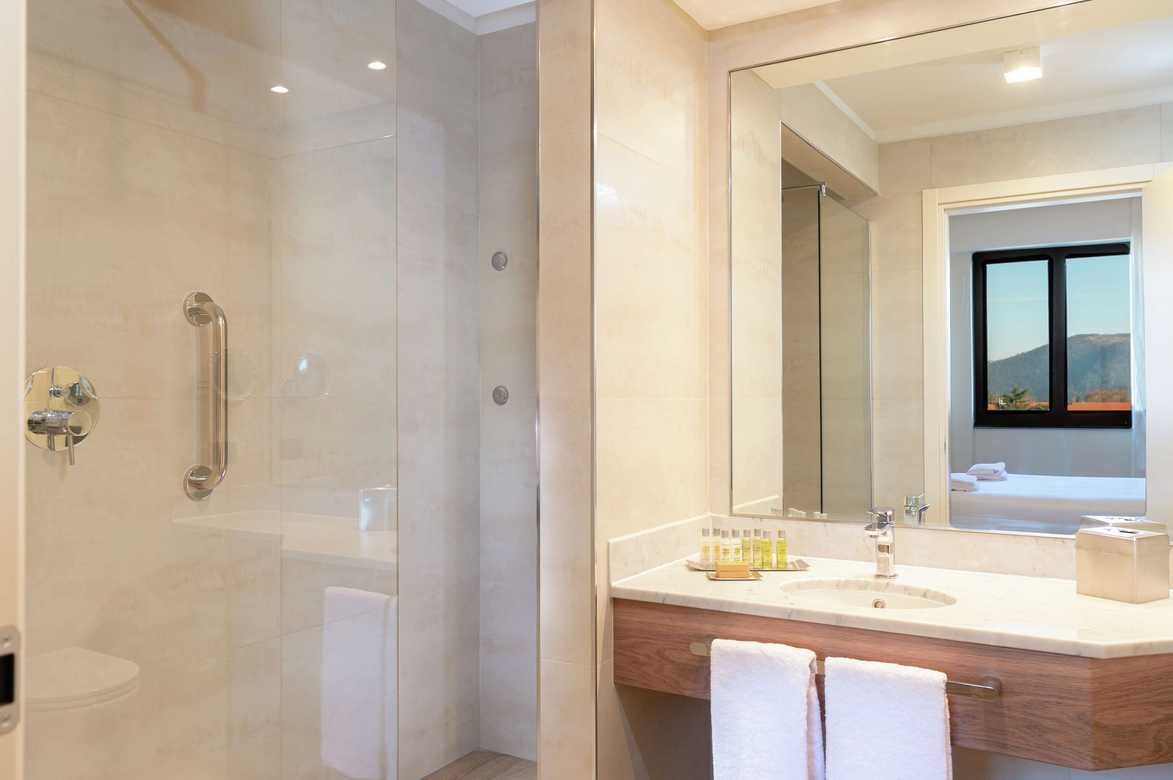 A modern bathroom with a glass-enclosed shower, a large mirror, and a vanity with a sink and towel rack.