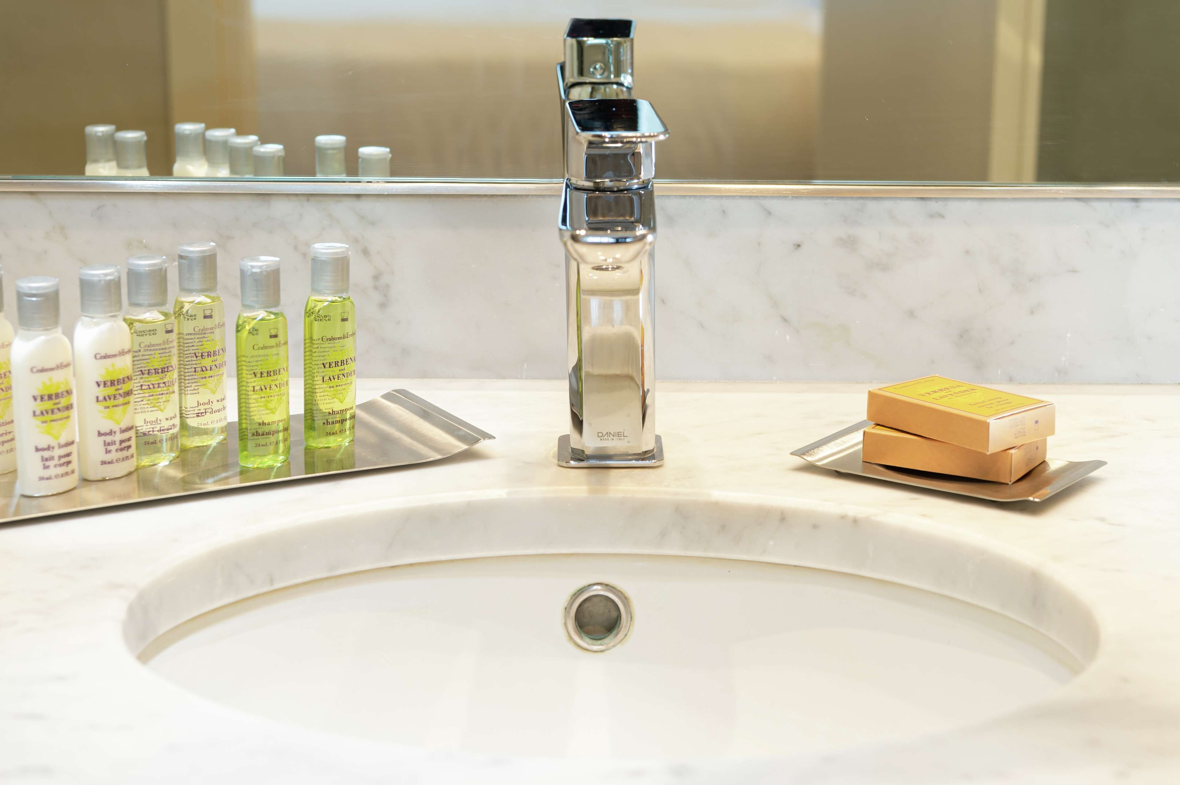 A bathroom sink with a chrome faucet, a mirror, and various toiletries including body lotion and shampoo bottles.