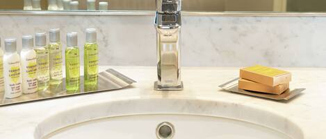 A bathroom sink with a chrome faucet, a mirror, and various toiletries including body lotion and shampoo bottles.