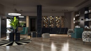 A modern lobby with a marble floor, a central plant, a seating area with patterned chairs, and a bookshelf filled with books. - DoubleTree by Hilton Brescia (Brescia)