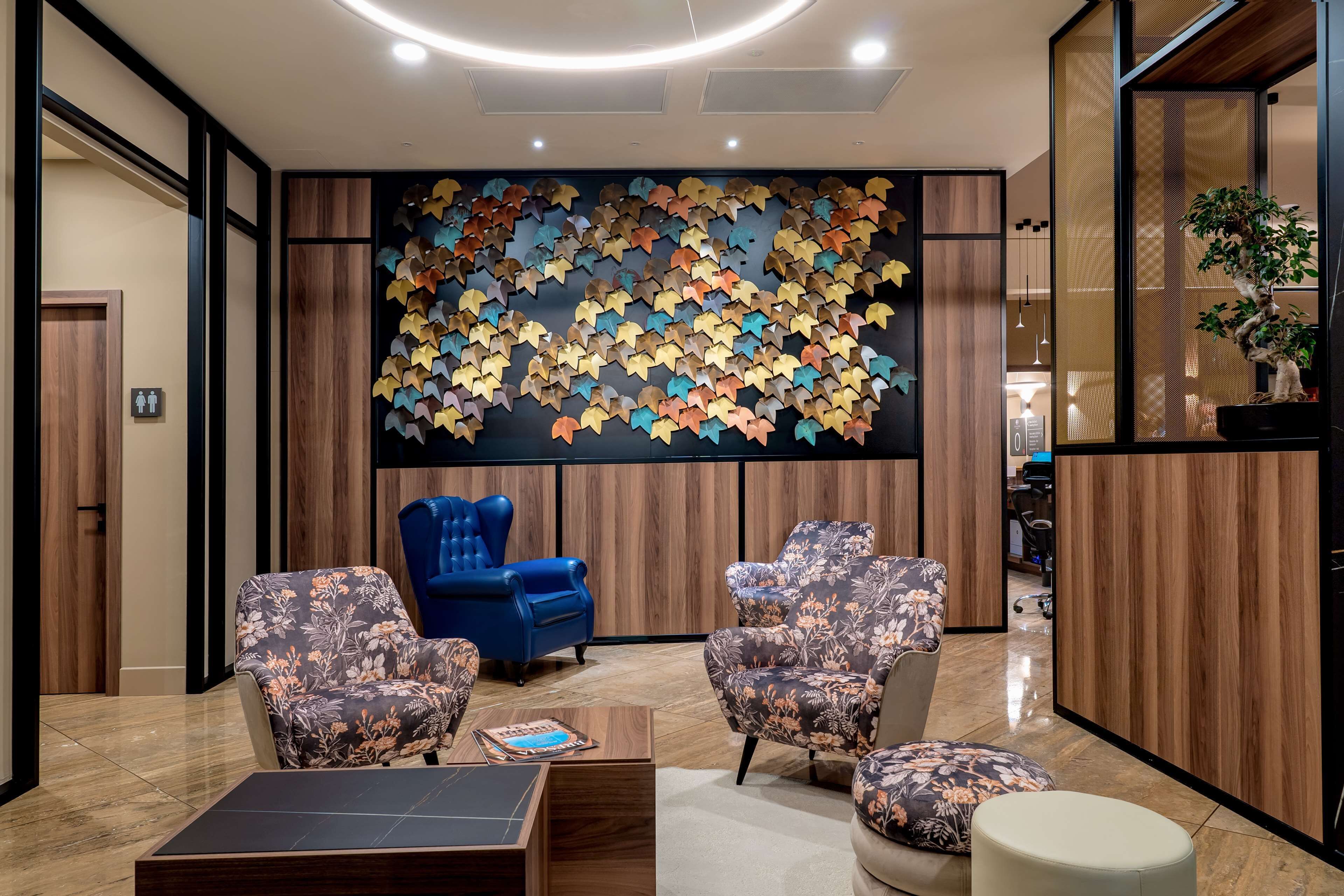 A modern lobby with a wooden panel wall, a blue armchair, floral-patterned armchairs, and a coffee table.