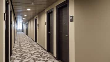 A long, narrow hallway with a patterned carpet, dark doors, and numbered room signs.