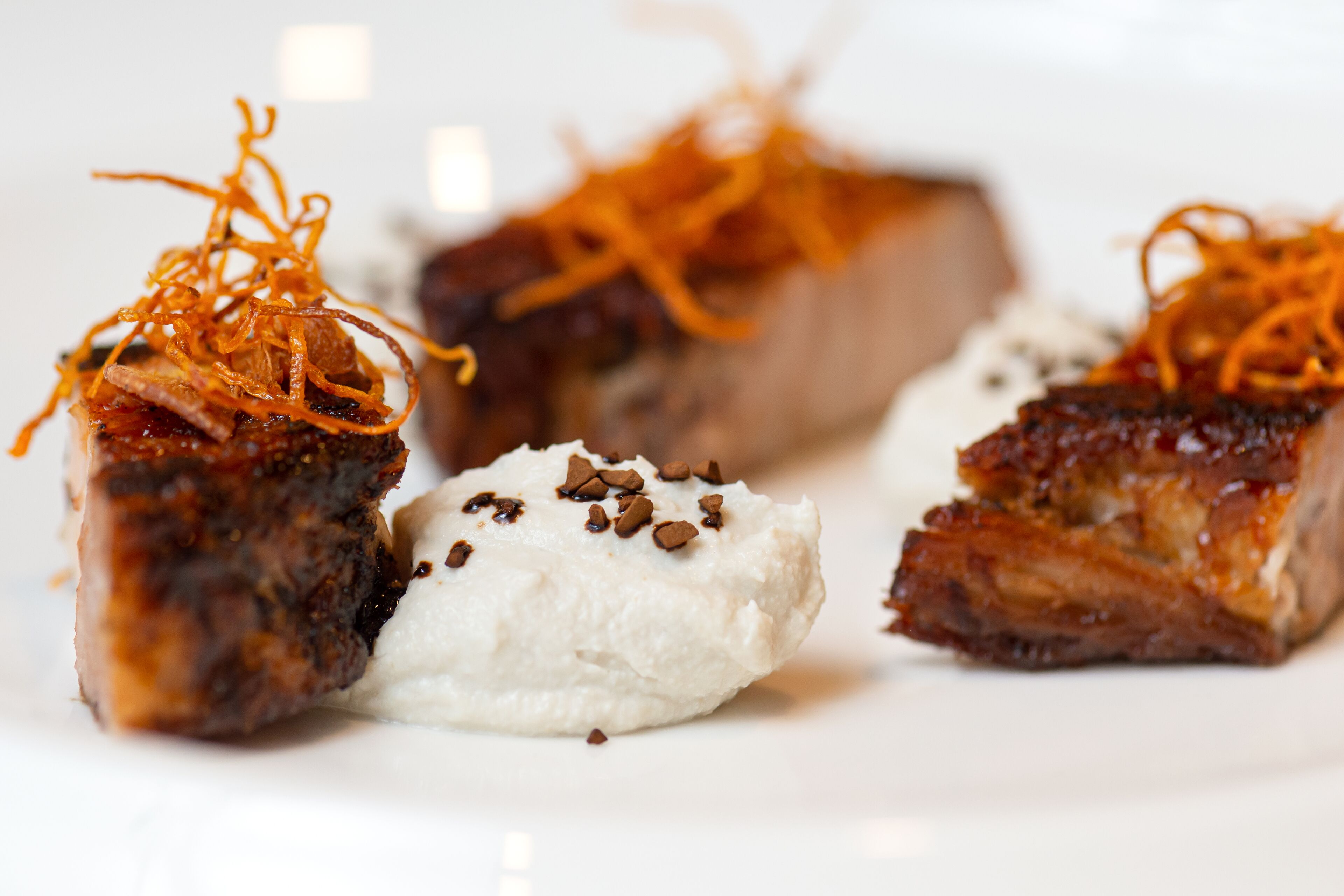 Un plato con tres trozos de carne y una porción de comida blanca, posiblemente helado o postre, adornado con ralladura de naranja.