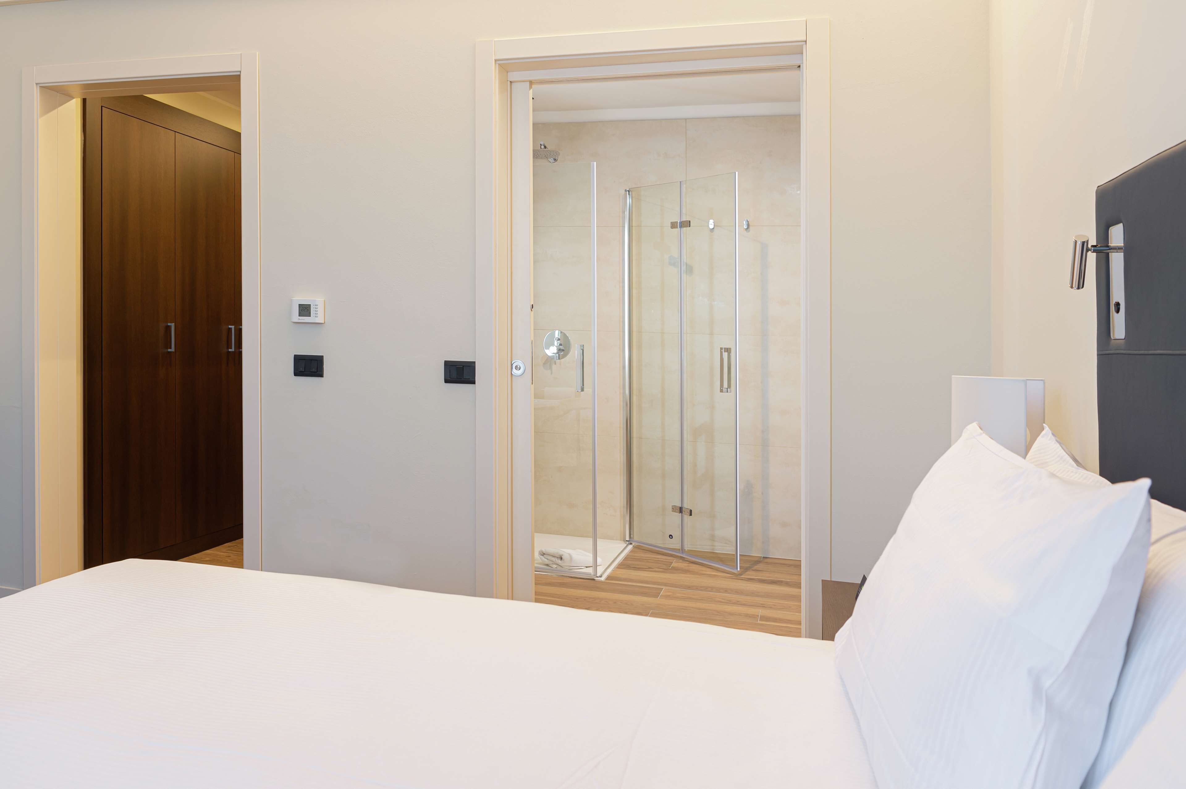 Ein Hotelzimmer mit einem Bett, einem Holzschrank, einer Duschkabine aus Glas und einem grauen Schrank.