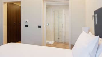 Una camera d'albergo con un letto, un armadio in legno, un box doccia in vetro e un guardaroba grigio.