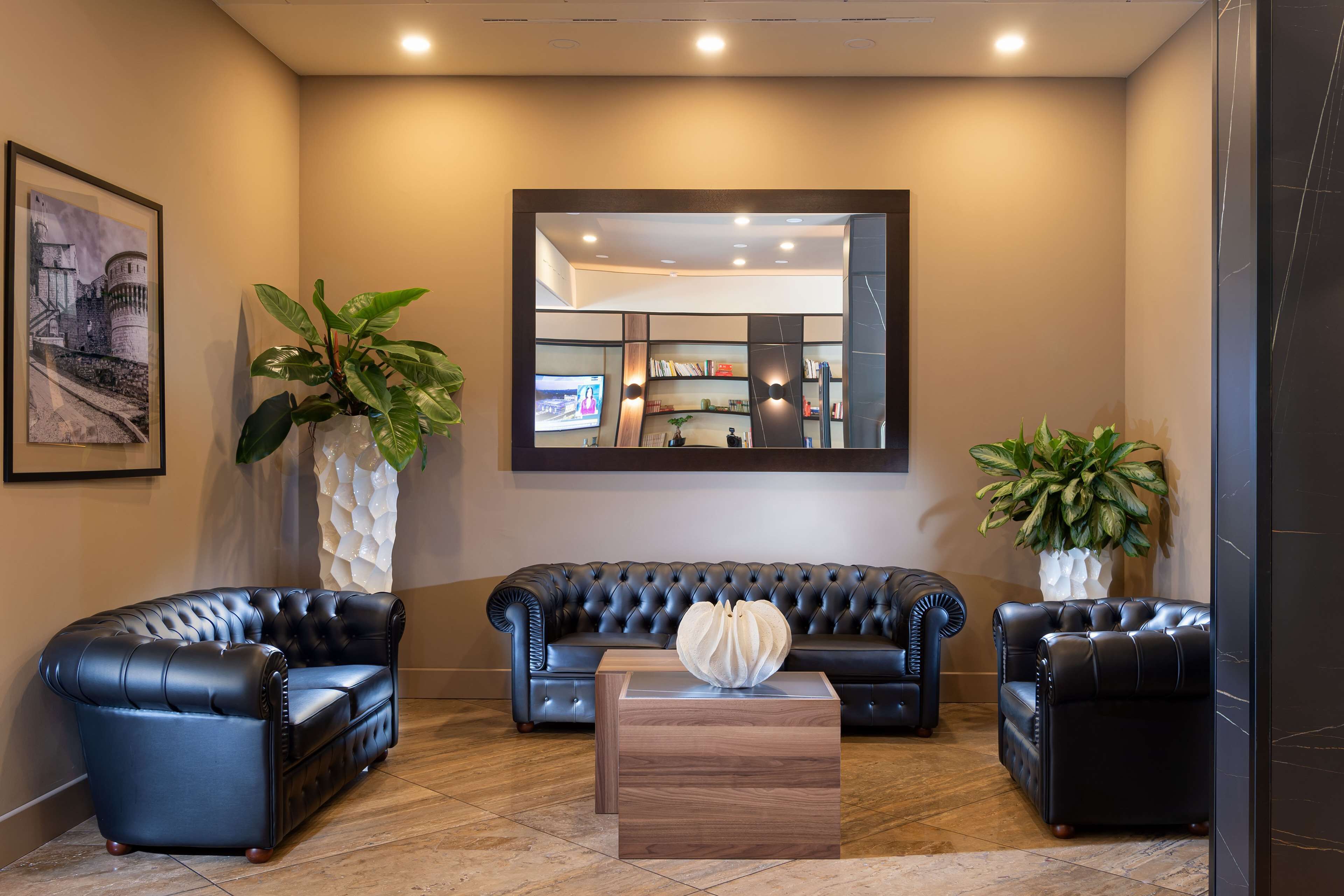 Een moderne lobby met een zwarte leren bank, twee fauteuils, een houten salontafel en grote potplanten.