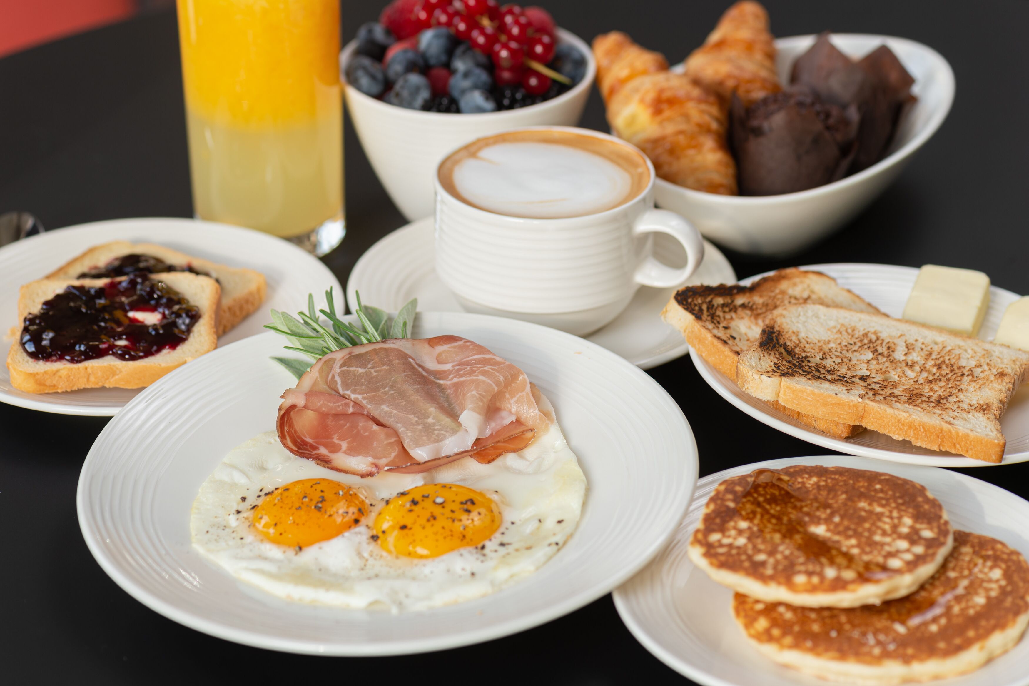 A breakfast table with toast, eggs, croissants, and a coffee cup.