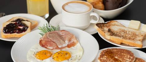 Una mesa de desayuno con tostadas, huevos, cruasanes y una taza de café.