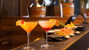 Two cocktails on a bar counter with a wooden background and a blurred bar area in the background.
