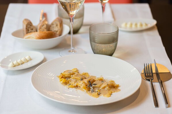A dining table with a plate of pasta, a bowl of bread, and a glass of wine. - DoubleTree by Hilton Brescia (Brescia)