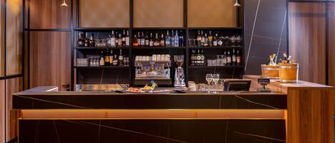 Una zona de bar con encimera de mármol, estanterías llenas de botellas de licor y lámparas colgantes.