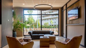 A modern lobby with a leather sofa, two armchairs, a wooden coffee table, and a large TV on the wall. - DoubleTree by Hilton Brescia (Brescia)