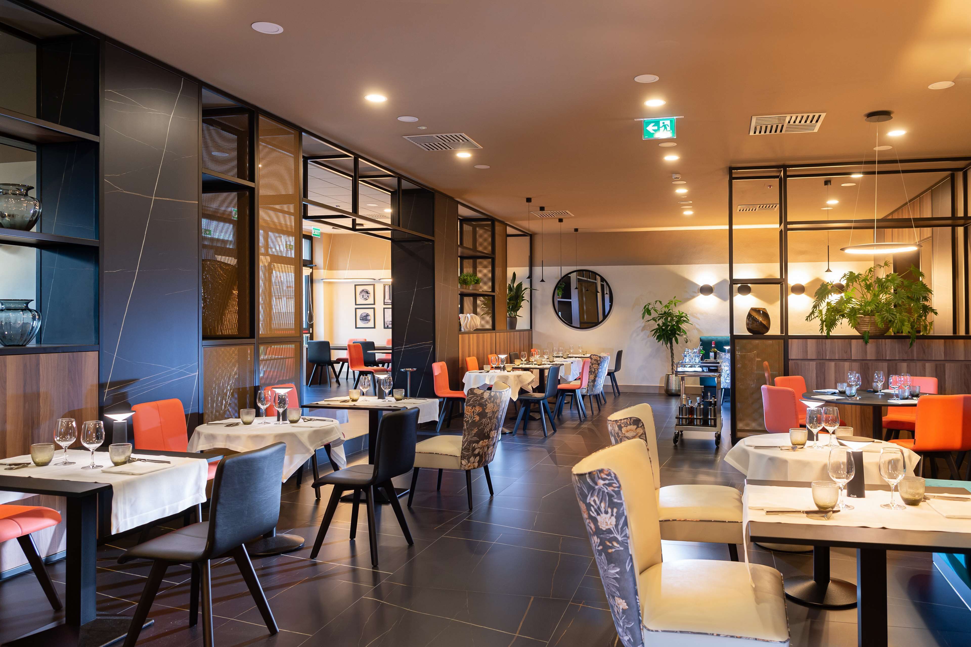 Un restaurante con mesas dispuestas para comer, sillas y una variada decoración que incluye plantas y obras de arte.