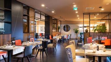 Un restaurante con mesas dispuestas para comer, sillas y una variada decoración que incluye plantas y obras de arte.