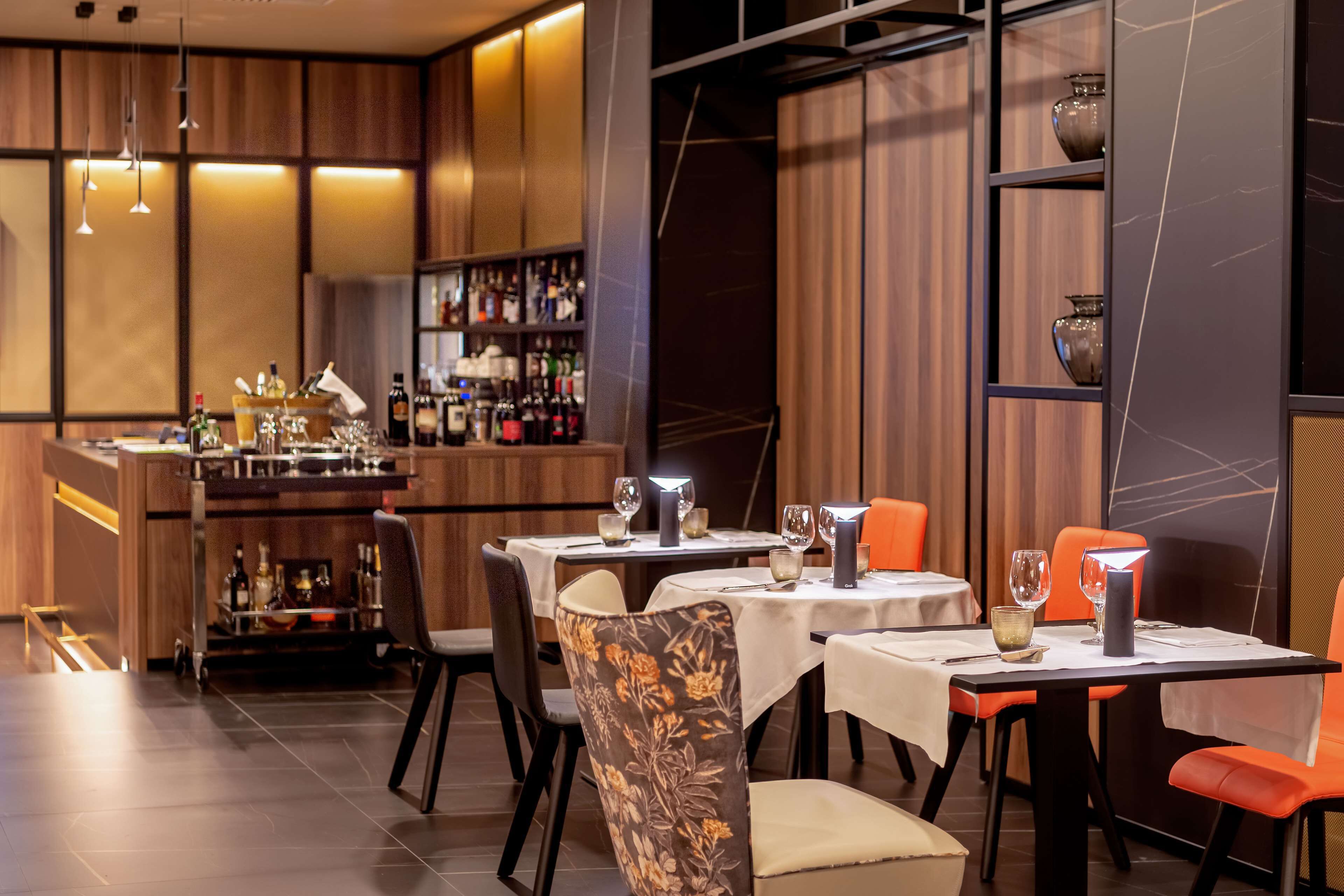 A restaurant with tables set for dining, a bar area with bottles, and a decorative wall.