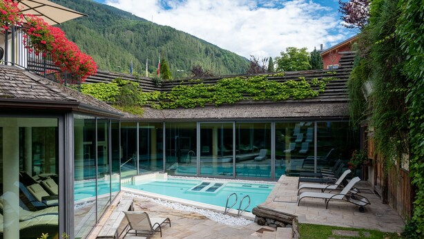 Un área de piscina exterior moderna con paredes de vidrio, sillas de descanso y un sendero de piedra.